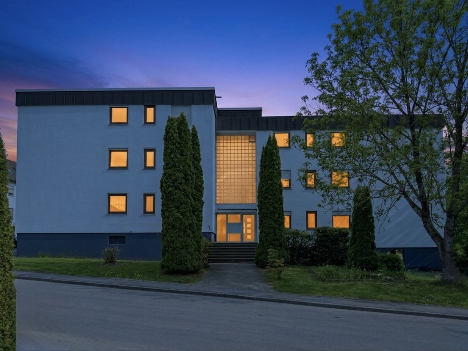 Twilight Immobilienfotografie Stuttgart, Mehrfamilienhaus mit beleuchtetem Eingang zur blauen Stunde